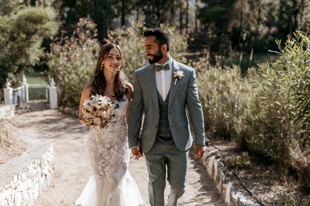 a man and woman in wedding attire holding hands and walking down a path